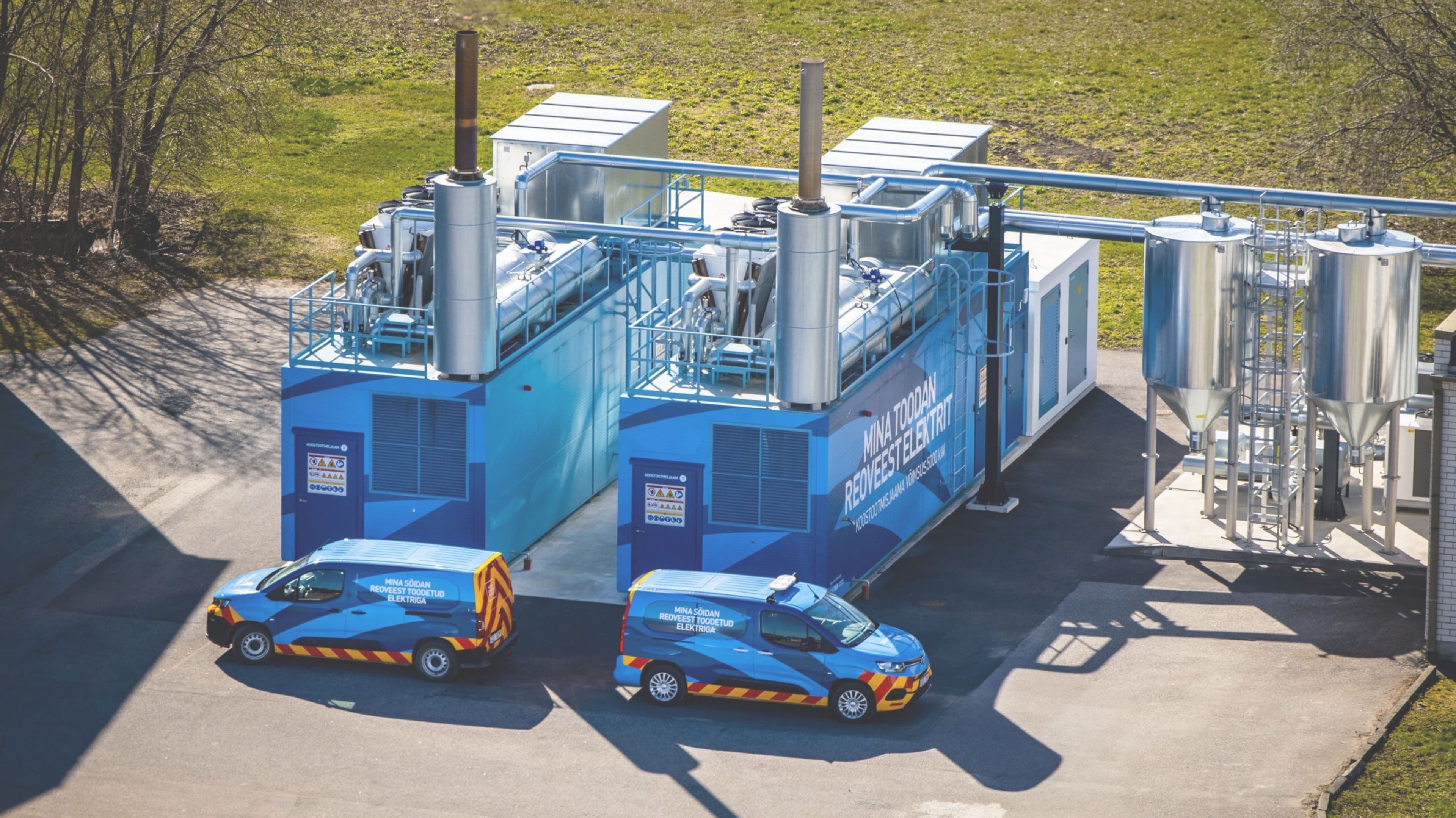 Two blue and white industrial processing units with two vans parked in front.