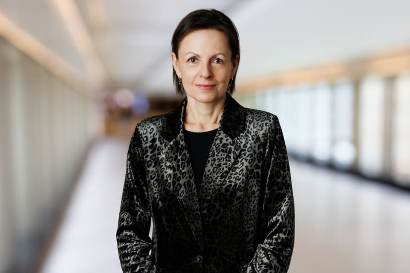 Woman with short dark hair wearing a textured black blazer in a modern setting.