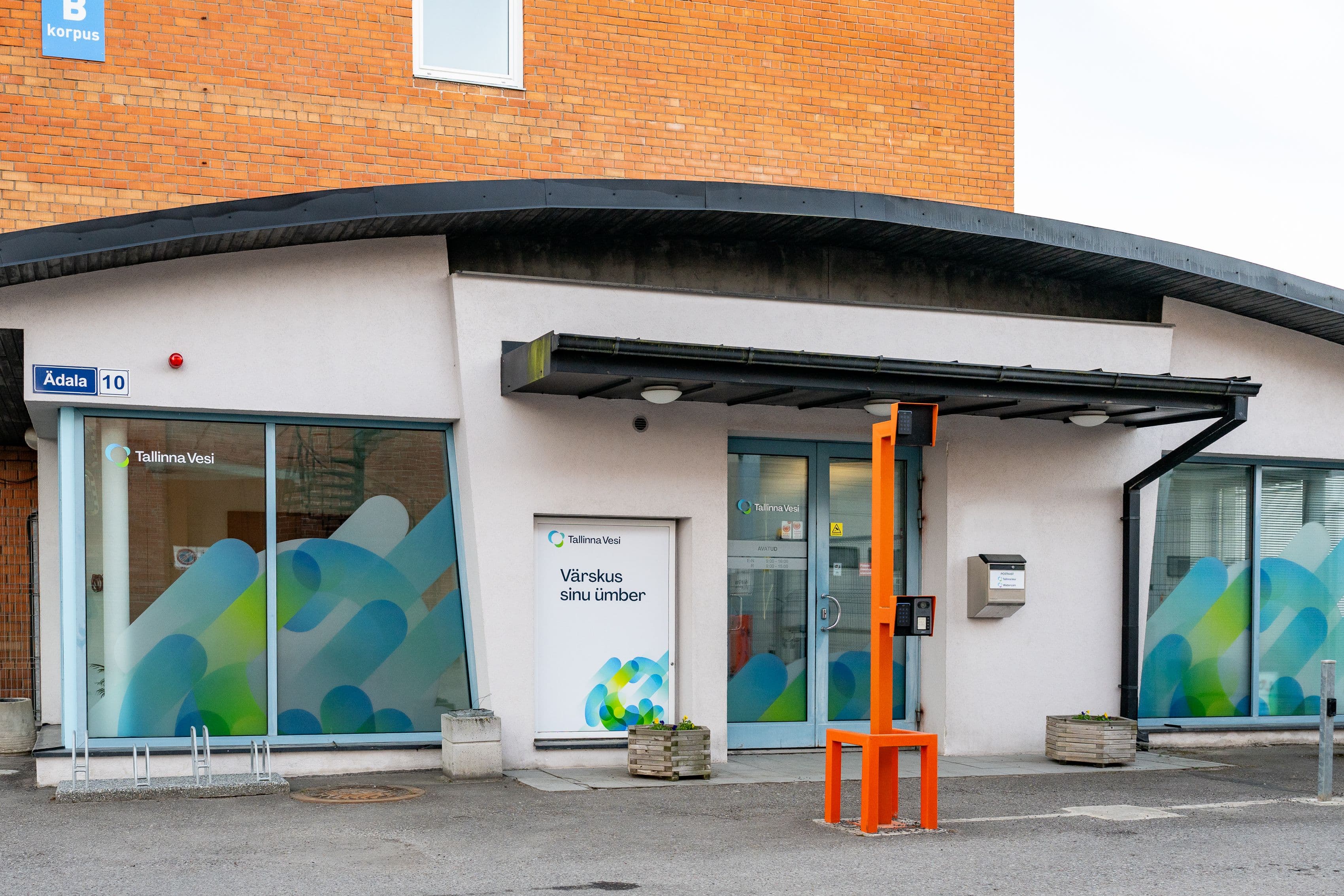 Modern building facade with abstract blue-green window decals and an orange structure at the entrance.
